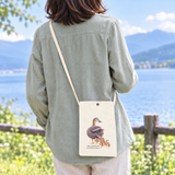 いきもの細密画アートグッズの帆布製サコッシュ。薮内正幸によるカルガモの親子イラストが描かれたナチュラルカラーのミニバッグを肩掛けしている様子。